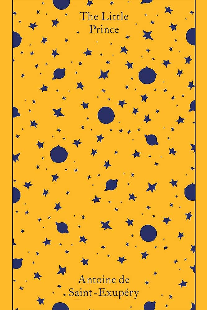 Book cover of 'The Little Prince' with a pattern of blue stars and planets on a yellow background.
